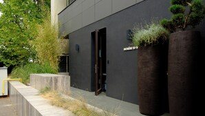 A modern building with a dark facade, a visible entrance, and large cylindrical planters with greenery. - Room12 (Bucharest)