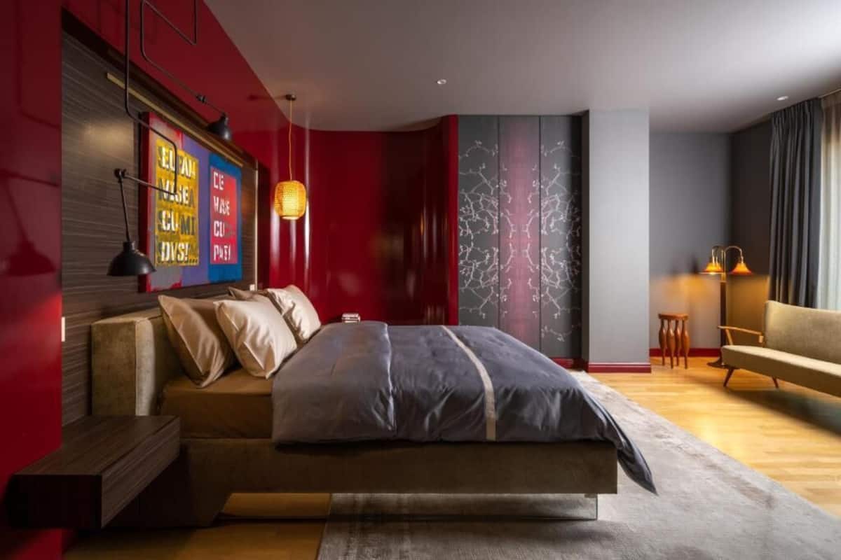 A modern bedroom with a bed, bedside tables, a red accent wall, and a marble-patterned wall.
