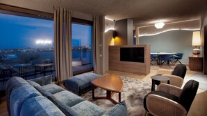 A modern hotel room with a large window offering a city view, a flat-screen TV, a dining area, and a cozy seating arrangement. - Room12 (Bucharest)