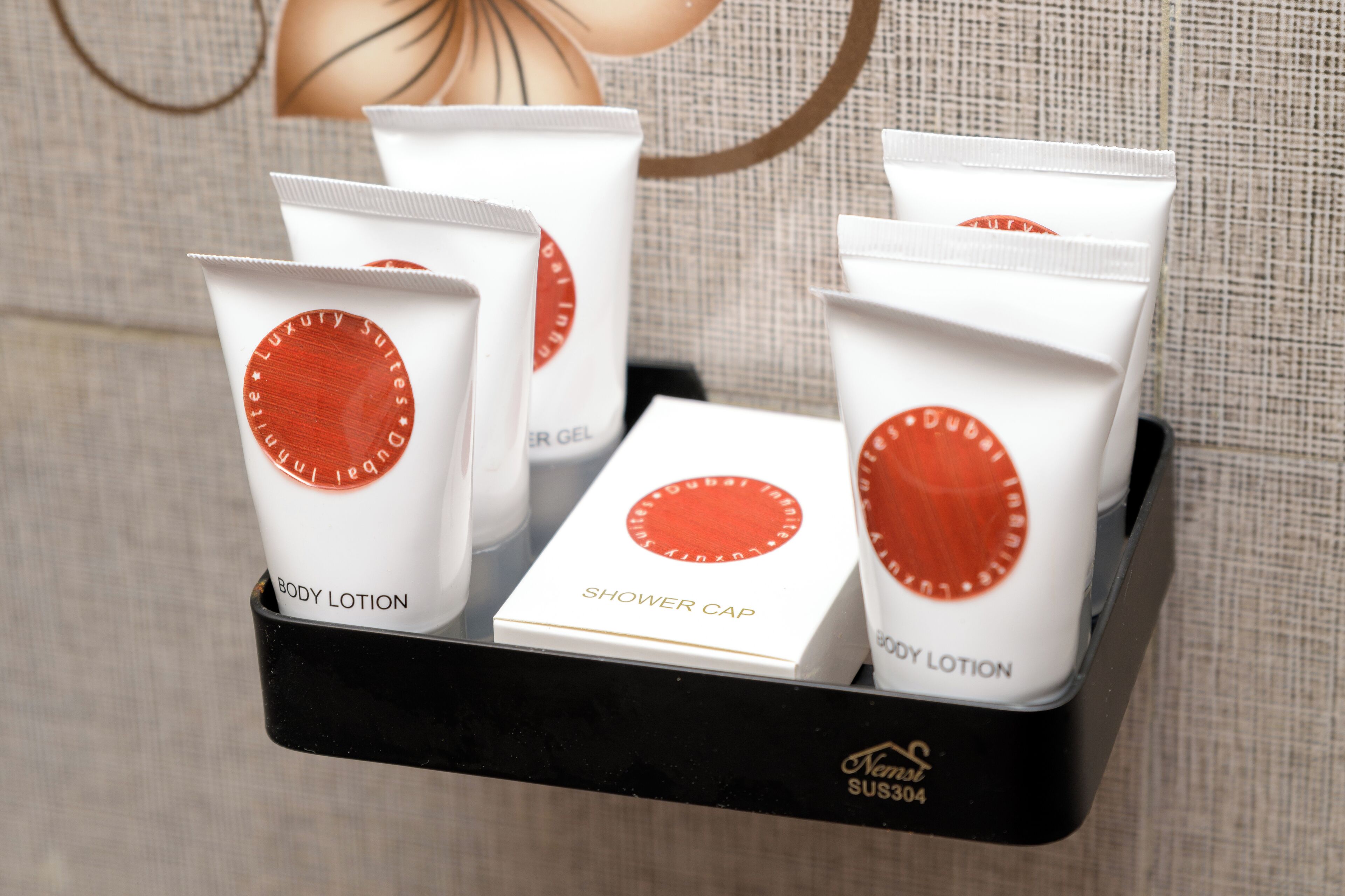 A black tray holding several white toiletry bags with red circular labels, including body lotion and shower cap.