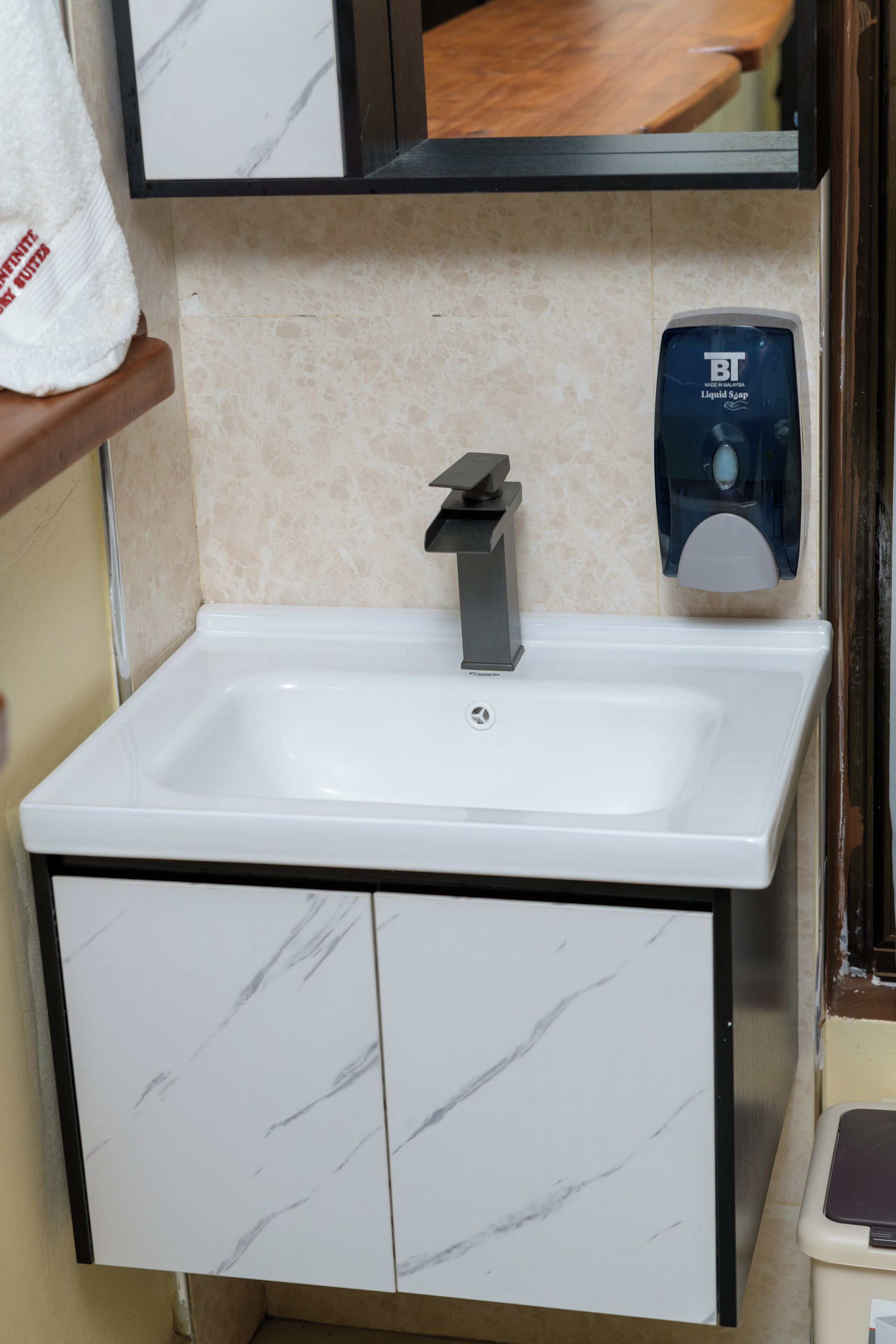 Un lavamanos con mueble de mármol debajo, un dispensador de jabón y un espejo encima.