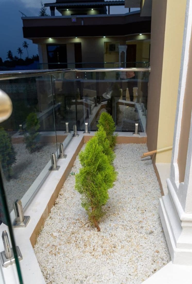 Ein Balkon mit Glastrennwand, ein kleiner Baum und ein Kiesweg.