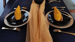 Una mesa de comedor decorada para un evento formal, con vajilla negra y dorada, un centro de mesa con tulipanes rojos y un arco de globos que dice 'Happy Birthday'.