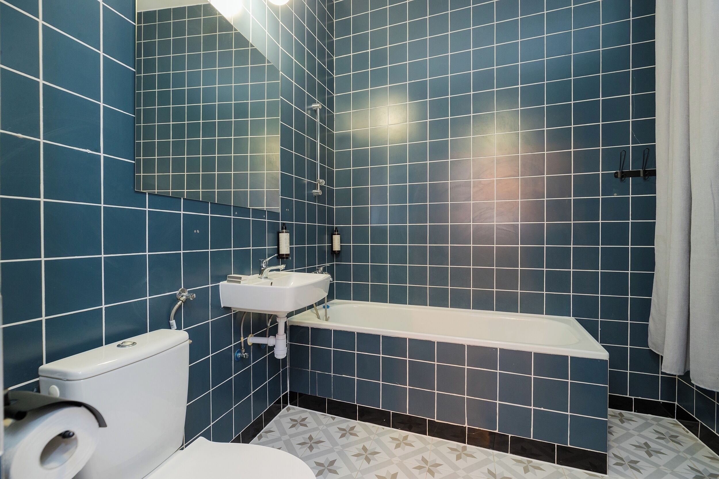 A bathroom with blue tiled walls, a white sink, a toilet, and a bathtub.