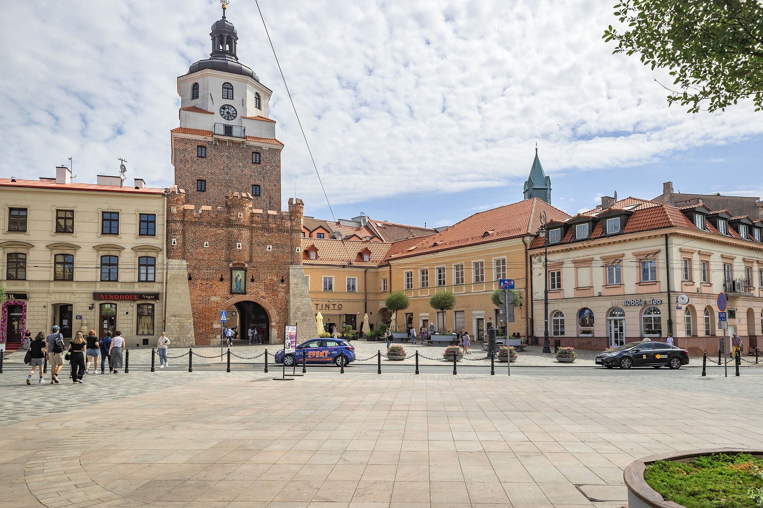 A public square with a prominent clock tower, surrounded by historic buildings and a clear sky.