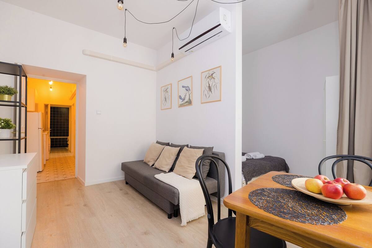 A modern living room with a sofa, a dining table with a fruit plate, and a staircase leading to another room.