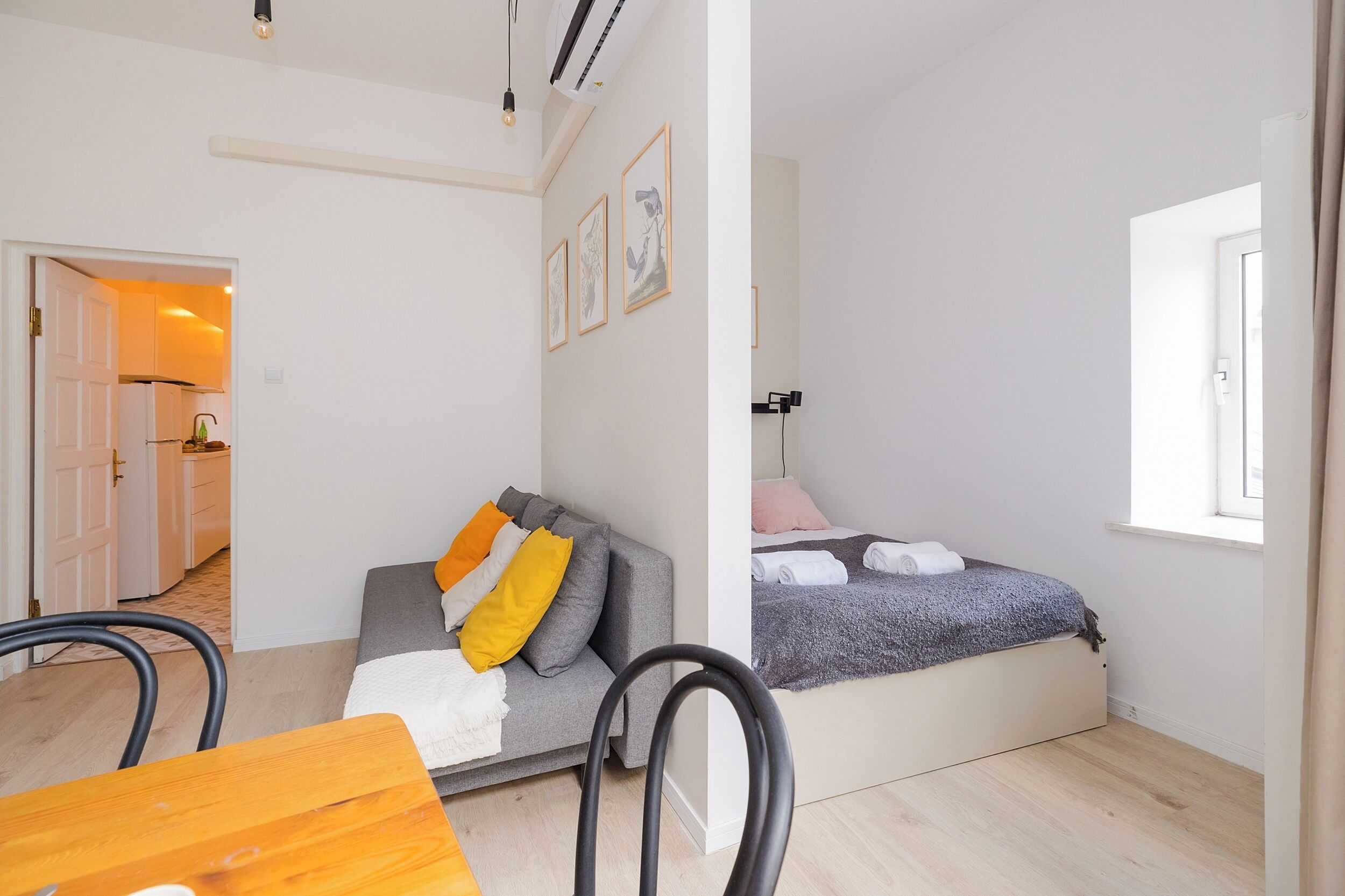 Una habitación funcional con cama, sofá, mesa de comedor y zona de cocina al fondo.