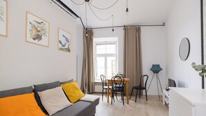 A modern living room with a grey sofa, yellow and white cushions, a dining table with chairs, a floor lamp, and a large window with curtains. - ShortStayPoland Krakowskie Przedmieście (Lublin)