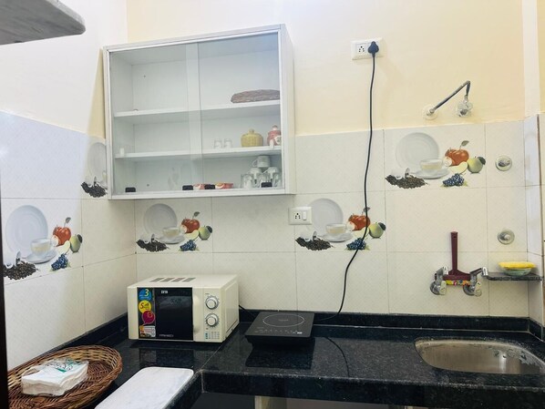 Una cocina con microondas, tostadora y pileta. En la pared, hay azulejos decorativos con diseños de frutas y verduras.