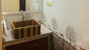 A bathroom with a large mirror, a sink with a decorative basin, and tiled walls with a deer and tree mural. - Bhanu Bhawan (Jaipur)