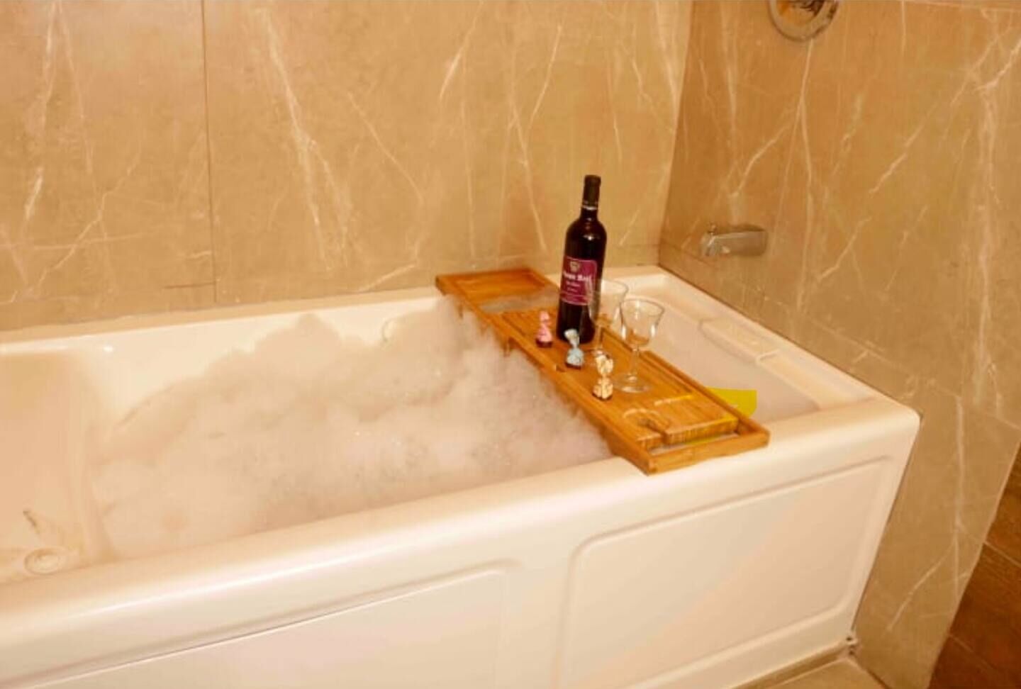 Une baignoire avec un plateau en bois sur lequel sont posés une bouteille et des verres.