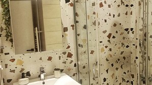 A bathroom with a glass shower enclosure, a white sink with a mirror above it, and a trash can. - Orsiida Deluxe House Volos (Volos)