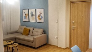 A living room with a sofa, a dining table, and a wooden floor. There are ceiling lights and a door in the room. - Orsiida Deluxe House Volos (Volos)