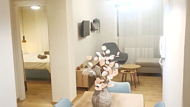 A modern dining area with a wooden table and chairs, a vase with flowers, and a sofa in the background. - Orsiida Deluxe House Volos (Volos)