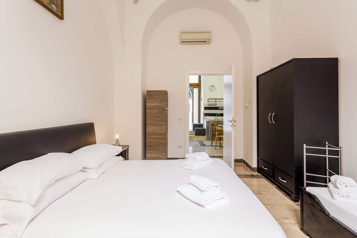 A hotel room with a large bed, a wardrobe, a desk, and a bathroom visible through an arched doorway.
