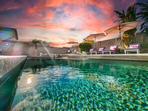A swimming pool with clear water, surrounded by lounge chairs and umbrellas, under a sunset sky. - Dream Home in Gilbert! Fun Times, Lots of Amenities! Pool Home. (Gilbert)