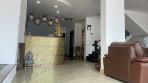 A spacious living area with a brown leather sofa, a decorative tiled column, and a reception desk with clocks. - Love Phu Quoc Hotel (Phu Quoc)