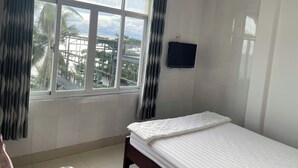 A bedroom with a large window, a bed, a flat-screen TV, and a view of palm trees and buildings outside. - Love Phu Quoc Hotel (Phu Quoc)