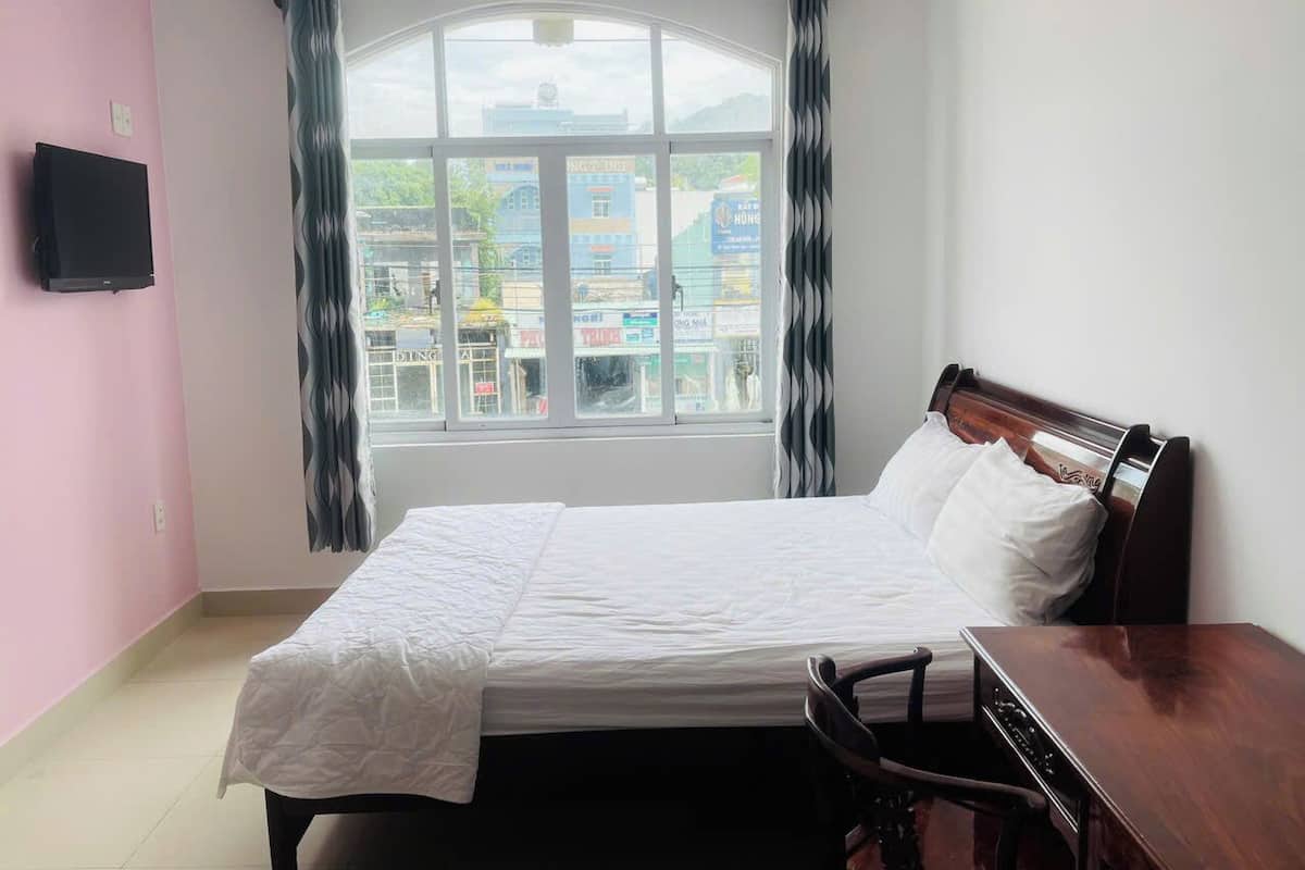 A bedroom with a bed, a desk, and a TV on the wall.