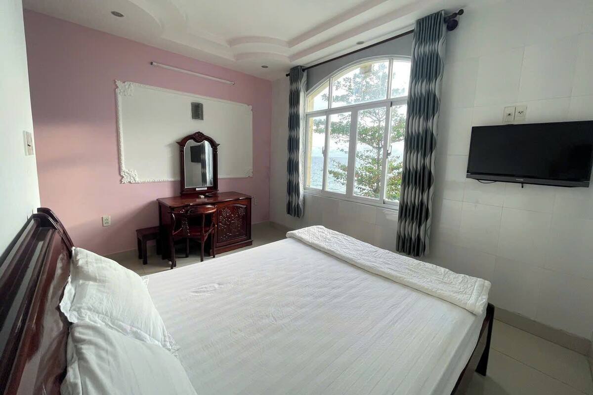 A bedroom with a large bed, a dresser, a mirror, and a TV on the wall.