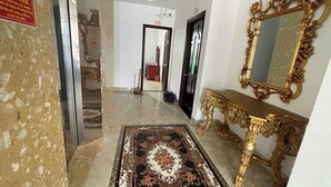 A hallway with a marble floor, a decorative rug, a golden ornate console table, and a large ornate mirror. - Love Phu Quoc Hotel (Phu Quoc)
