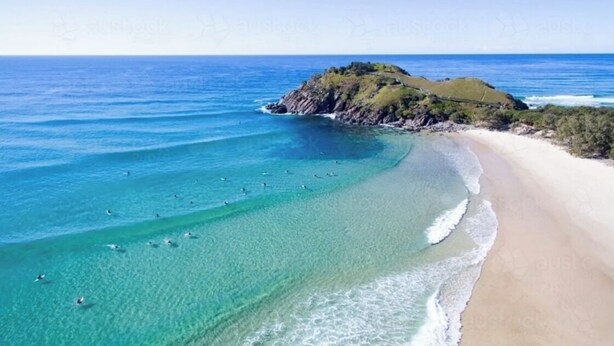 A coastal beach with clear turquoise waters, a sandy shore, and a small hill with vegetation.