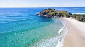 Una playa costera con aguas turquesas cristalinas, una orilla arenosa y una pequeña colina con vegetación.