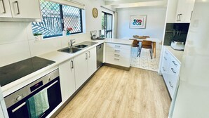 A modern kitchen with white cabinets, a wooden countertop, a built-in oven, and a window with a decorative screen.
