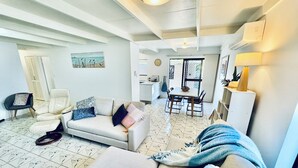 A spacious living area with a sofa, a chair, a dining table, and a kitchen in the background.