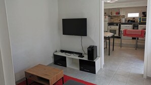 A modern living room with a flat-screen TV mounted on the wall, a wooden coffee table, and a red rug. - 1 bedroom house 800m from the sea (Saint-Raphaël)
