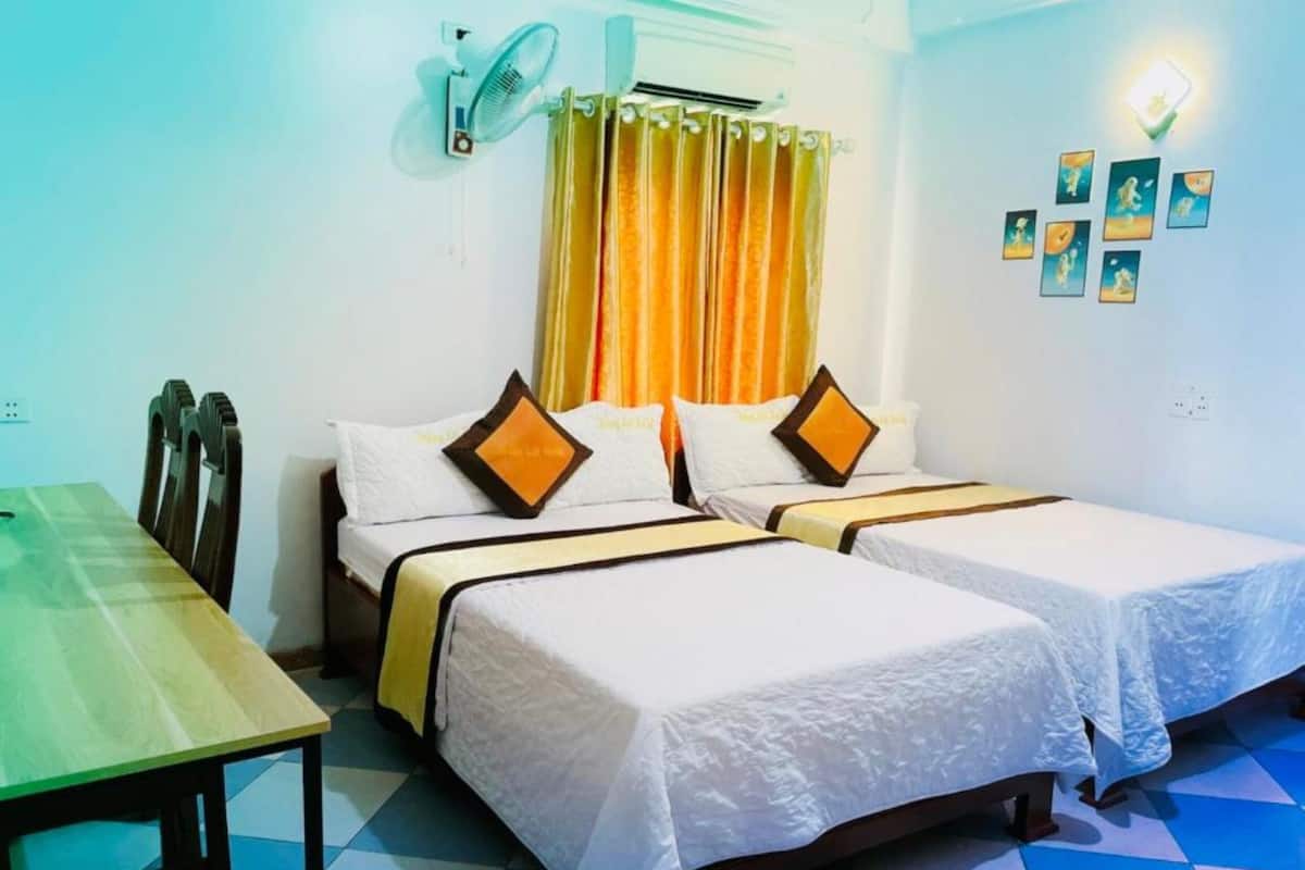 Une chambre d’hôtel avec deux lits, une table et un ventilateur.