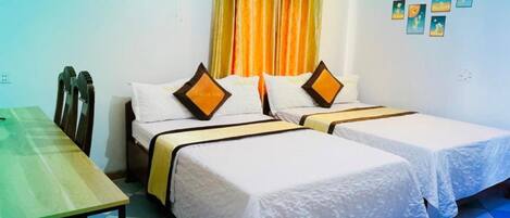 A hotel room with two beds, a table, and a fan.