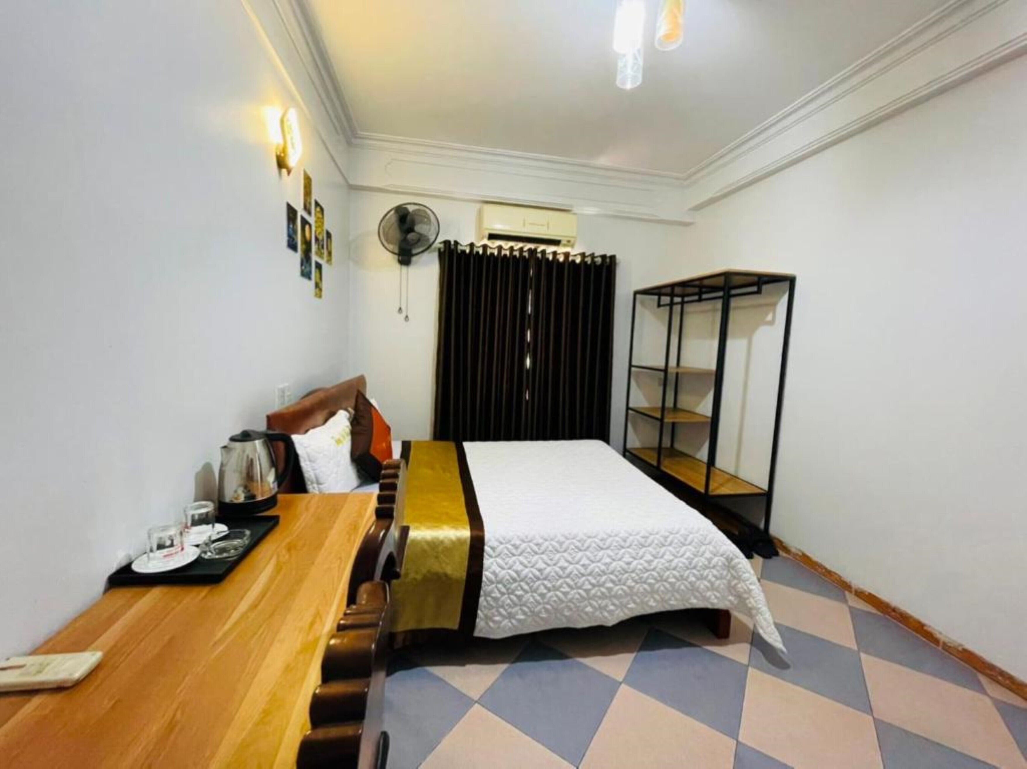 Una habitación de hotel con cama, una mesa de madera, un ventilador y un armario.