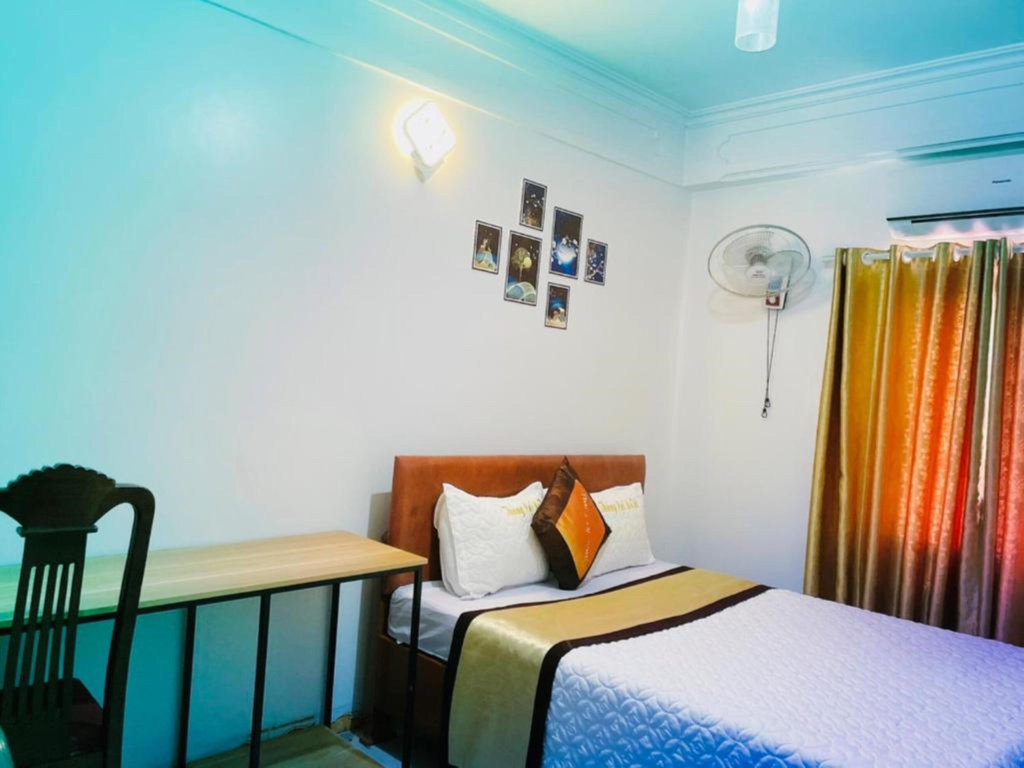 A bedroom with a bed, a desk, a chair, a wall-mounted fan, and a curtain.