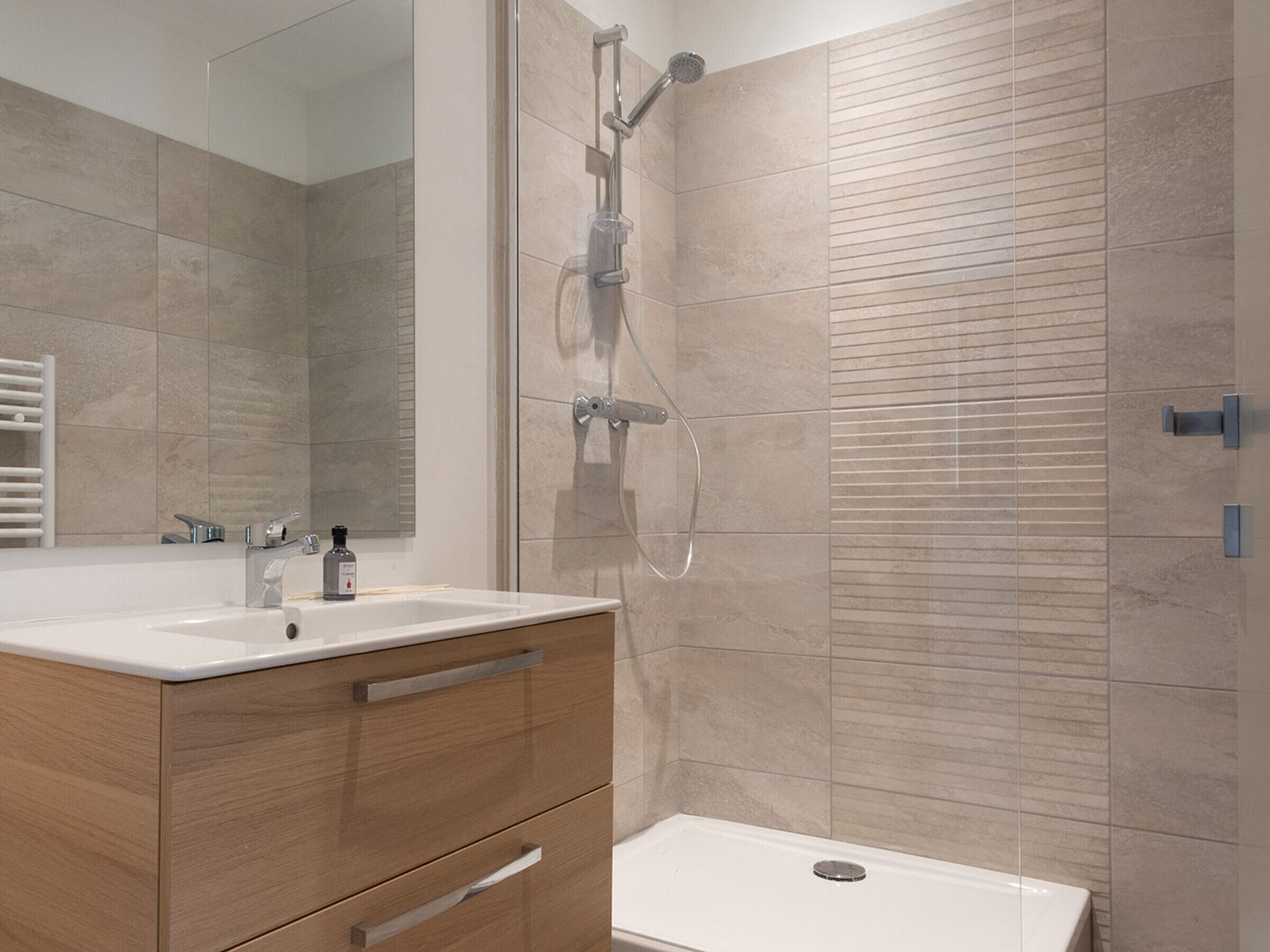 A modern bathroom with a large mirror, two sinks, a shower, and wooden cabinetry.