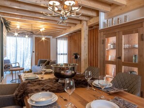 Un intérieur en bois avec une table à manger dressée pour six personnes, un lustre et un plaid en fourrure posé sur la table.