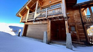 A wooden chalet with a balcony, a garage door, and a snowy landscape. - Luxury 4* Chalet with Jacuzzi and Sauna (Vars)