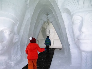 A person in a red jacket and another in a blue jacket walking through an ice tunnel with large ice sculptures. - Luxury 4* Chalet with Jacuzzi and Sauna (Vars)