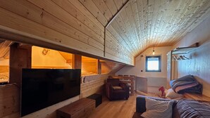 A cozy attic bedroom with a wooden ceiling, a large TV, a bed, and a small seating area with a chair and a table. - Studio Vars, studio flat, 4 persons (Vars)