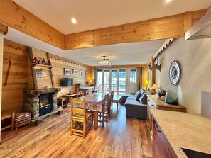 A cozy log cabin interior with a dining area, fireplace, and a large window overlooking the outside. - T3 Apt in Vars Center, Ideal for 6, Steps from Slopes (Vars)