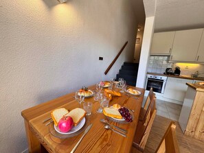 A dining table set with bread, cheese, grapes, and an apple, with a kitchen in the background. - Apartment at the Slopes near ESF (Vars)