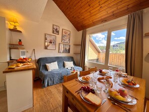 A cozy room with a sofa, dining table set with food, a TV, and a window with a view.