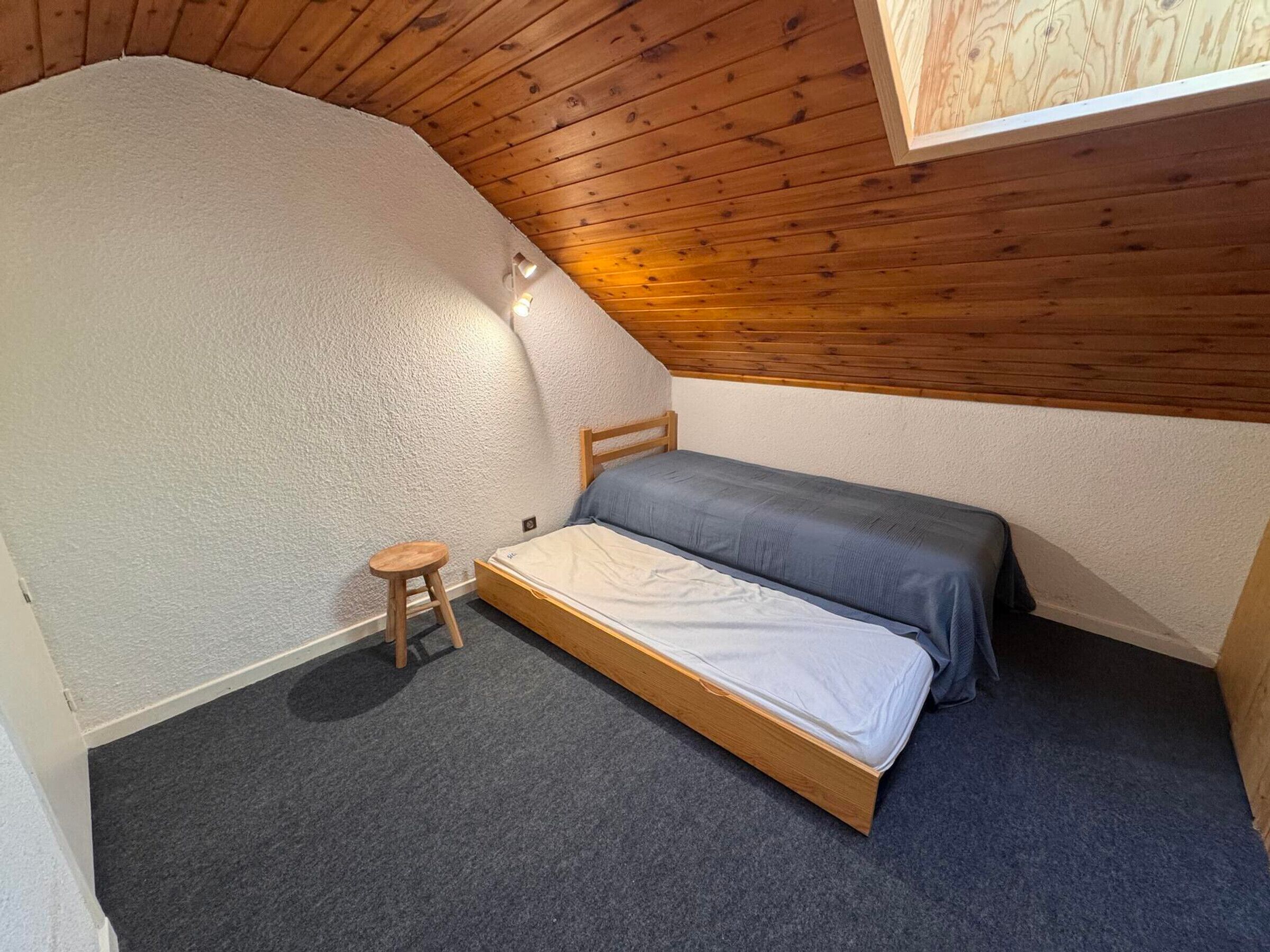 A small, single-bed room with a sloped ceiling and wooden paneling.