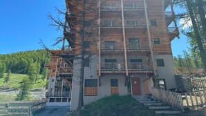 Um edifício de madeira com vários andares, varandas, uma entrada central e uma escadaria que leva à porta principal.