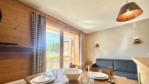 A wooden dining table set with plates, cutlery, and glasses, a blue sofa, and a hanging pendant light. - Apartment Vars, 1 bedroom, 4 persons (Vars)