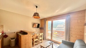 A cozy cabin with a wooden interior, a dining area, a sofa, and a large window offering a view of a mountain. - Apartment Vars, 1 bedroom, 4 persons (Vars)