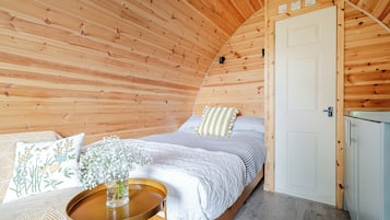 A cozy bedroom with a wooden ceiling, a bed with striped bedding, a bedside table with a vase of flowers, and a white door.
