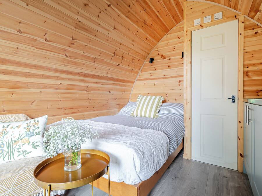 A cozy bedroom with a wooden ceiling, a bed with striped bedding, a bedside table with a vase of flowers, and a white door.