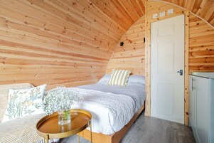 Un dormitorio acogedor con techo de madera, cama con ropa de cama a rayas, mesita de noche con un jarrón de flores y una puerta blanca.