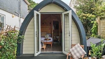 A cozy, semi-open cottage with a wooden interior, a small dining area, and a garden view.